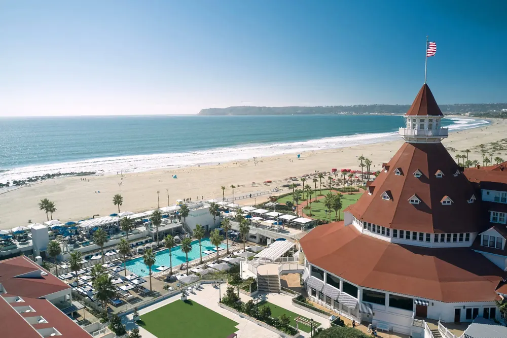 Aerial view of the red-roofed Hotel del Coronado turret and beachfront pool in Coronado