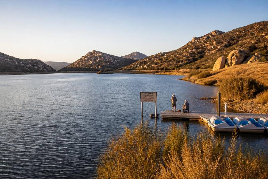 Anglers fishing from the dock at Lake Poway at golden hour with pedal boats moored and boulder hills behind
