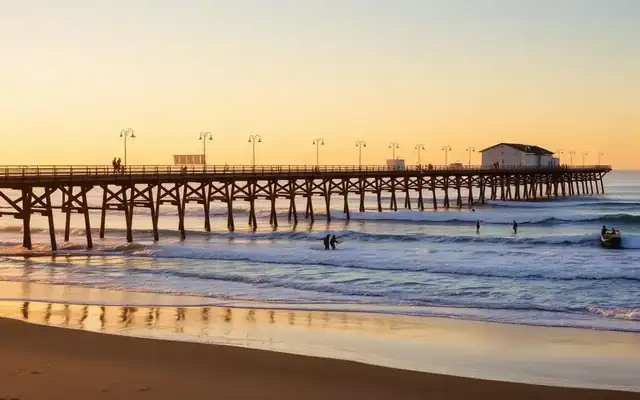 Long wooden Oceanside pier extending over the Pacific with surfers below
