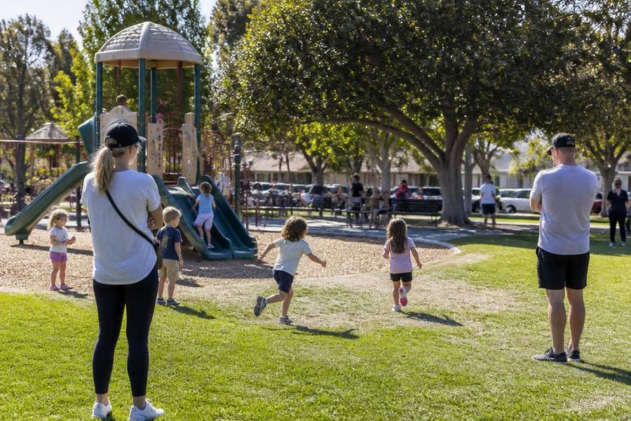 Children playing on a playground at a sunny suburban Poway community park with parents watching