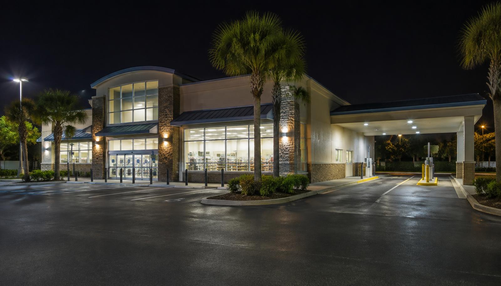 Drugstore lit up at night with an empty parking lot and palm trees