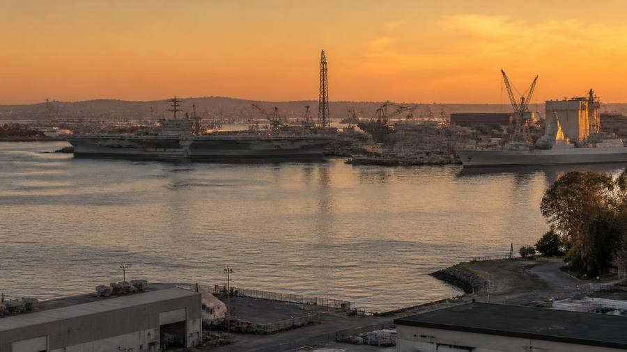 San Diego Bay shipyard at golden hour with naval vessels and shipbuilding cranes along the industrial waterfront