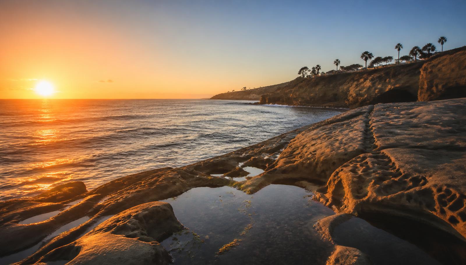 Golden hour light across a San Diego sandstone cove and tide pools with the sun low over the Pacific