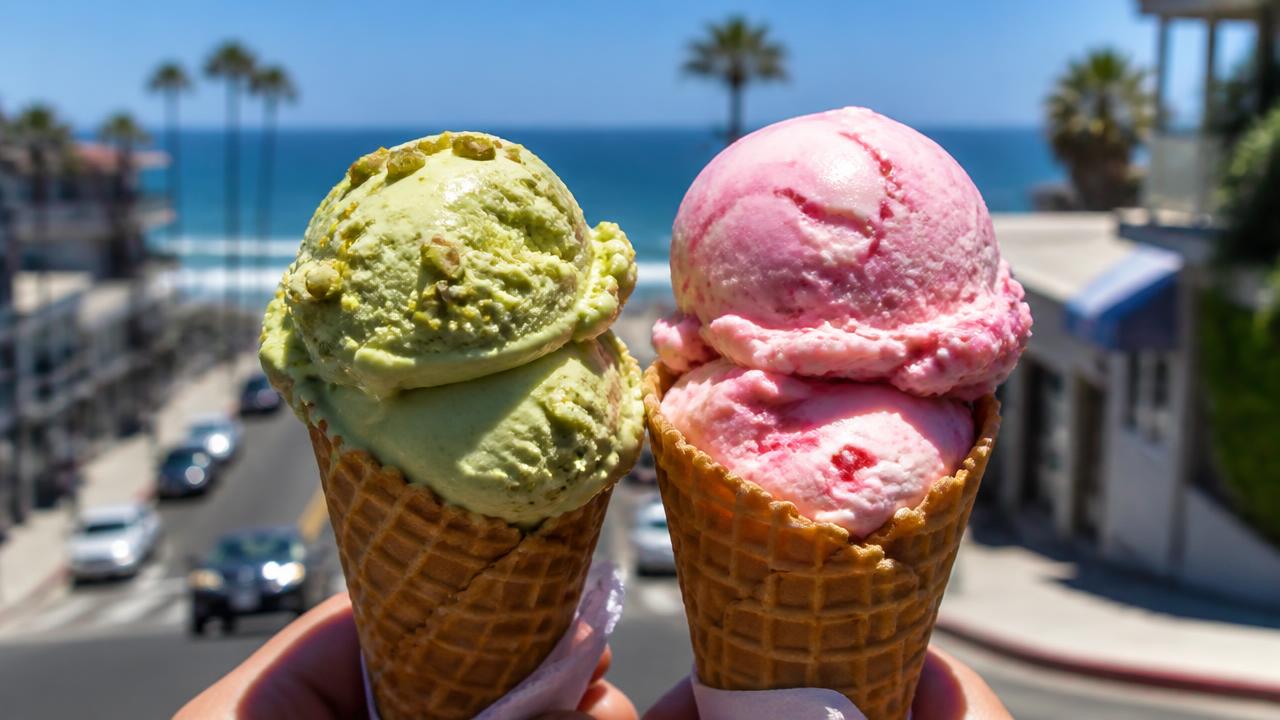 Two artisan ice cream cones with pistachio and strawberry scoops held up against a sunny San Diego beach street