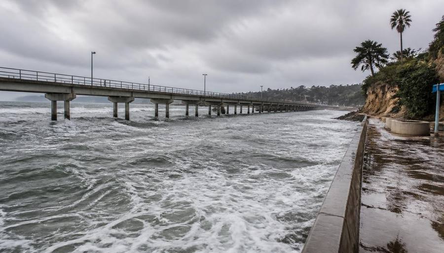 High surf flooding beneath Scripps Pier in La Jolla during a king tide with waves surging against the seawall