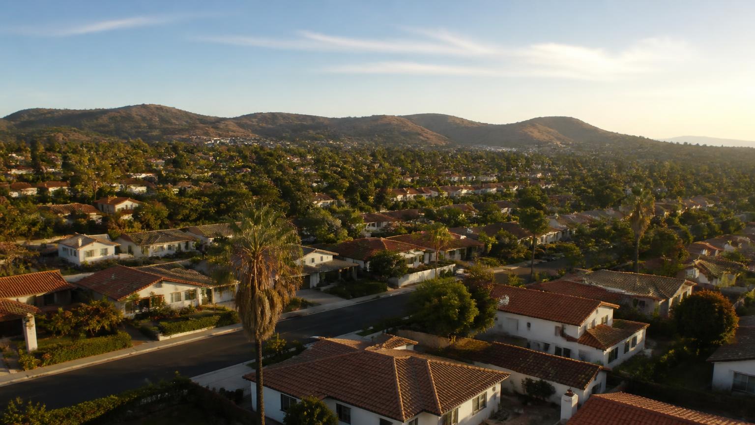 Aerial view of a San Diego residential neighborhood of stucco homes with red tile roofs and hills in the distance