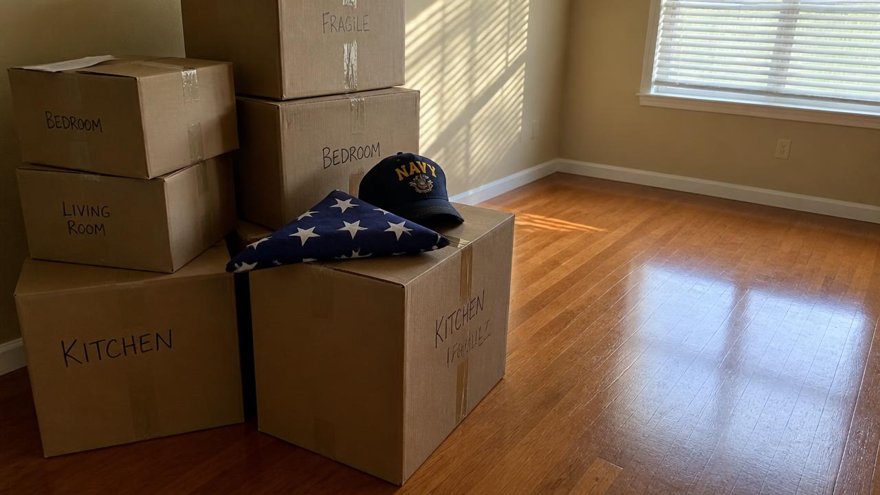 Labeled moving boxes with a folded American flag and Navy ball cap in an empty San Diego apartment