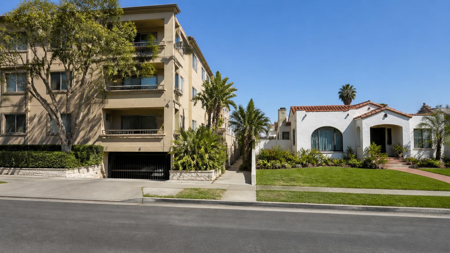 San Diego street with an apartment building on one side and a single-family stucco house with a lawn on the other