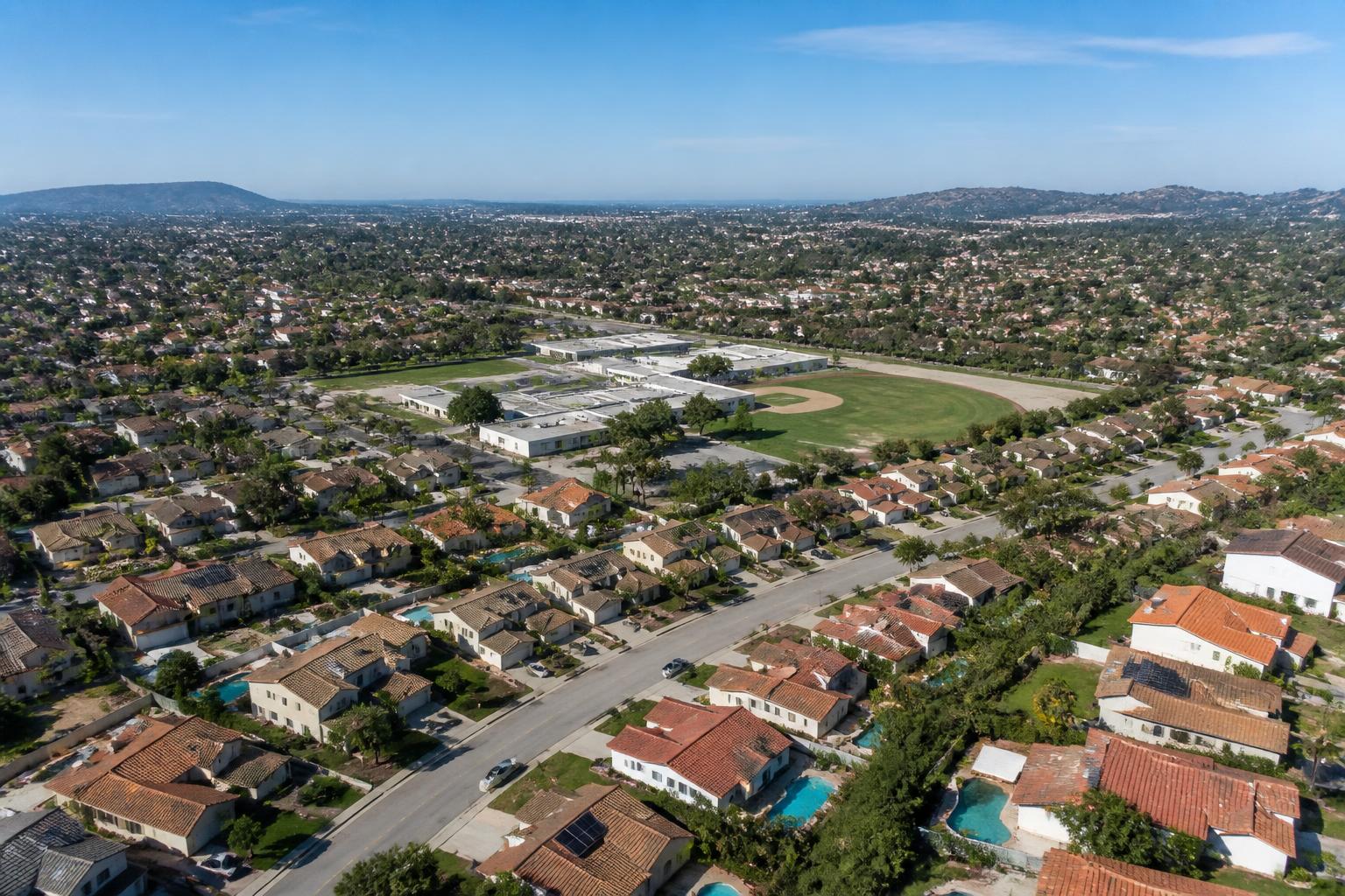Aerial view of a San Diego suburban neighborhood with tile-roof homes and a school campus with sports field