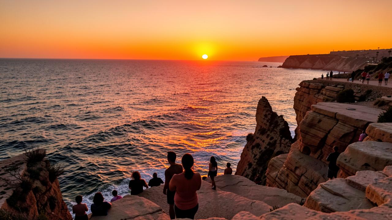 The sun setting into the Pacific Ocean viewed from sandstone cliffs in San Diego with silhouetted onlookers