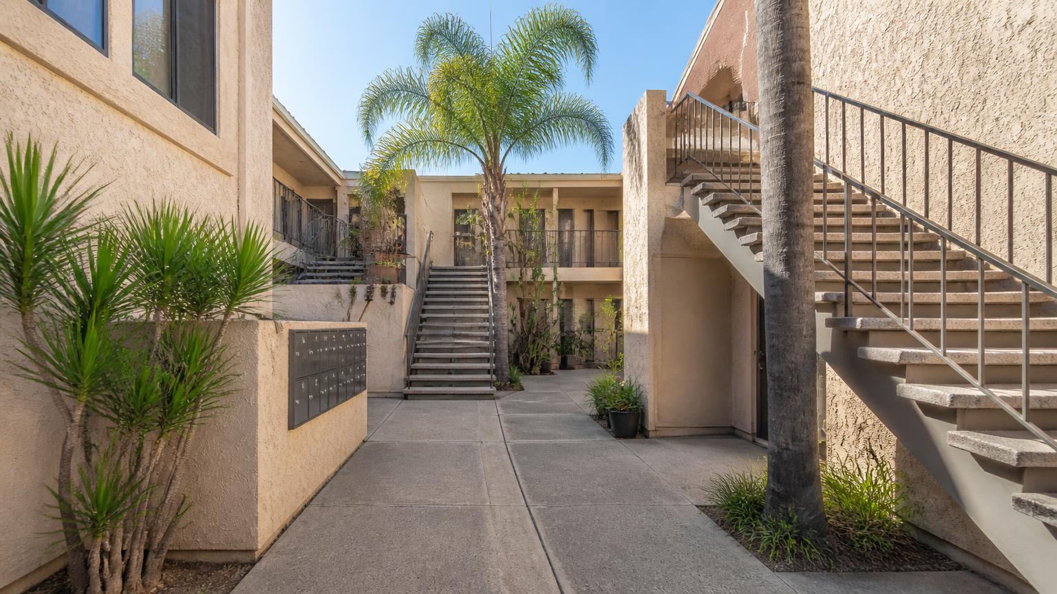 Sunlit courtyard of a stucco San Diego apartment building with exterior staircases, mailboxes, and palm trees