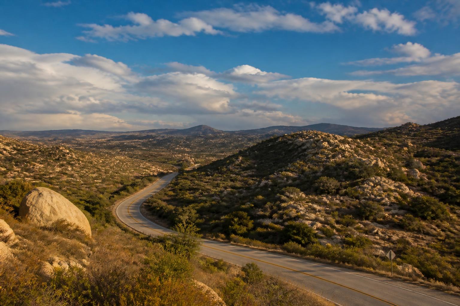 Two-lane highway winding through boulder-strewn East County San Diego backcountry hills in late afternoon light